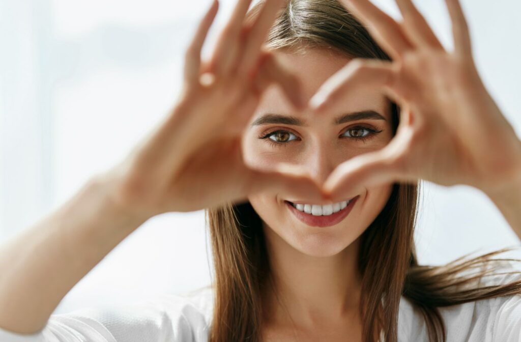 A woman smiling and making a heart shape with her hands, and the heart is surrounding her eyes