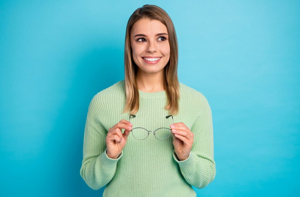 A woman smiling and taking off her glasses after she recovered from LASIK eye surgery
