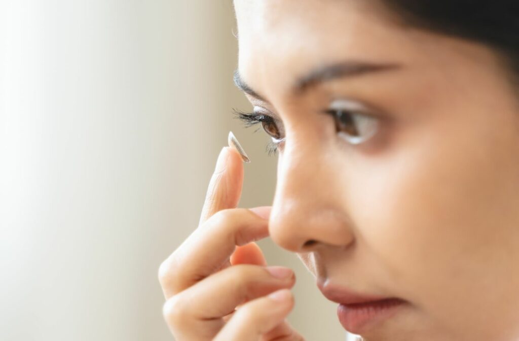 A close-up image of a woman placing a contact lens into her eye.