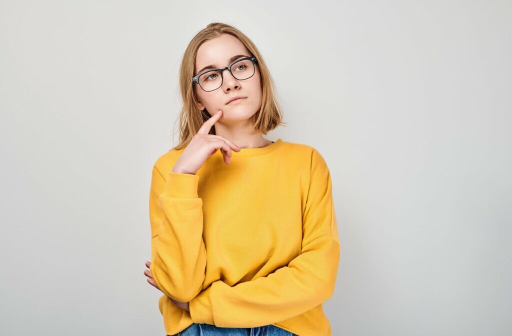 Young adult in a yellow sweater against a grey background wearing blue framed glasses wondering about LASIK surgery