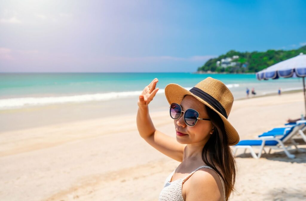 A young traveller at a beach protects their eyes from the sun by wearing a hat and sunglasses.