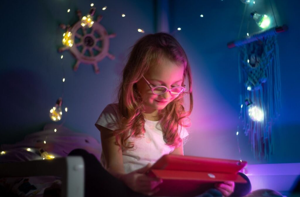 A child wearing glasses using a tablet under colorful lights highlighting the impact of screen time on vision