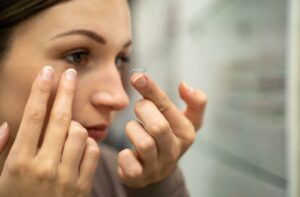 An adult places their trial lens in their eye after getting a contact lens fitting exam.