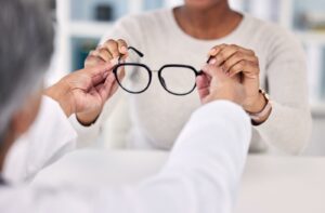 An eye care professional handing a pair of black-framed eyeglasses to a patient during a consultation.