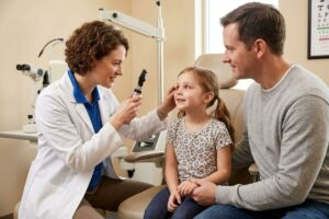 An optometrist examines the eyes of a child showing symptoms of pink eye.